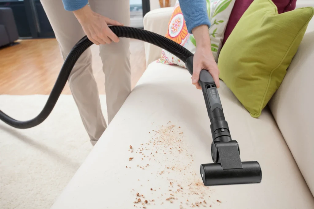 Close-up: Vacuuming up debris from a light-colored sofa.