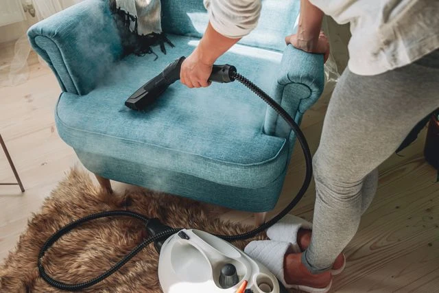 Woman steaming a blue armchair with a handheld steamer.
